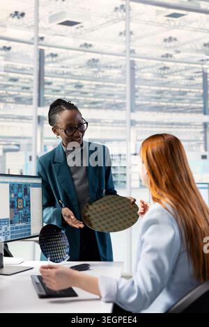 Assessing production quality, semiconductor substrates close up and women in microchip factory research facility. Working together, silicon wafer and female engineers in office studying materials Stock Photo