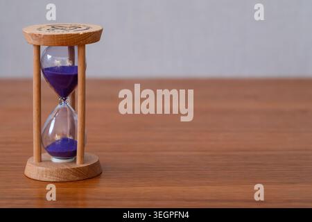 Wooden Hourglass with Purple Sand on Table with Large Copy Space, Background with Hourglass on Office Desk and Empty Space for Text Stock Photo