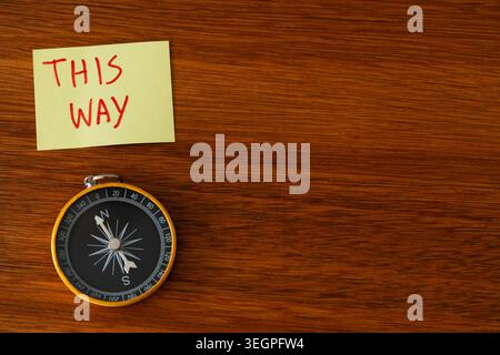 Compass and This Way Note on Wooden Background with Copy Space, Career Path and Strategic Direction Symbolism on Polished Wood Stock Photo