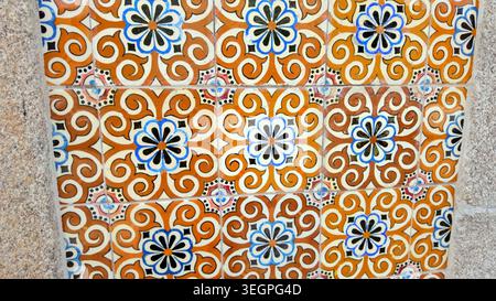 A close-up view of traditional Portuguese azulejo tiles featuring vibrant orange, blue, and black floral patterns set against a textured stone wall, c Stock Photo
