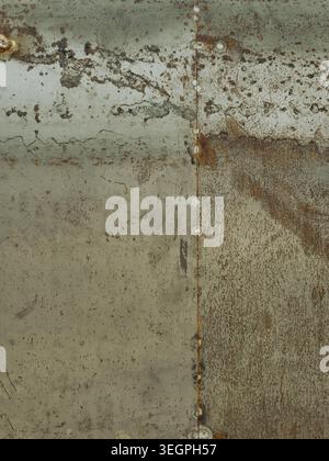 A vertical shot of a weathered metallic surface featuring a central weld line and heavy oxidation. The natural lighting highlights the rough gritty te Stock Photo