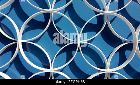 A high angle shot of a white architectural lattice featuring an overlapping circular design. Bright daylight creates sharp diagonal shadows against a Stock Photo