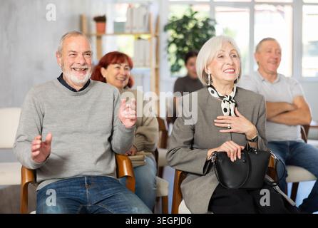 Cheerful and sociable group of students of different ages sitting on chairs, listening lecture and laughing in lecture hall Stock Photo