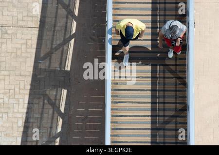 Top-down view of two cruise passengers walking up a gangway with long architectural shadows on the ground below. Stock Photo