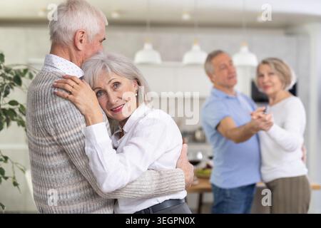 Two married couples enjoying slow dancing at house party for friends Stock Photo