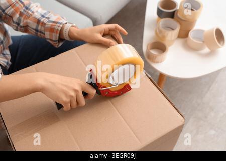 Young woman taping up cardboard box in living room on moving day, top view Stock Photo