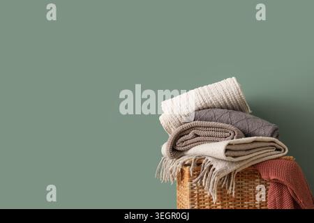 Wicker basket with stack of different cozy blankets on turquoise background Stock Photo
