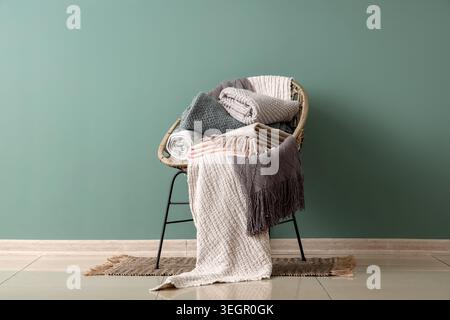 Wicker chair with different cozy blankets near turquoise wall in room Stock Photo