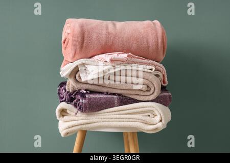 Stack of different cozy blankets on chair against turquoise background Stock Photo