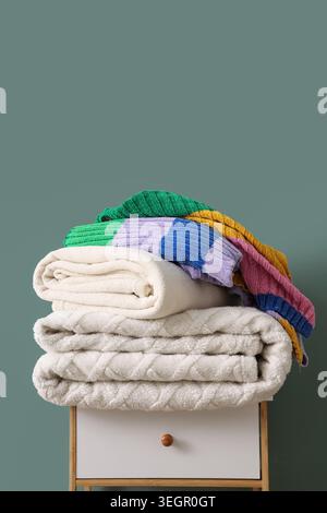 Stack of different cozy blankets on bedside table against turquoise background Stock Photo