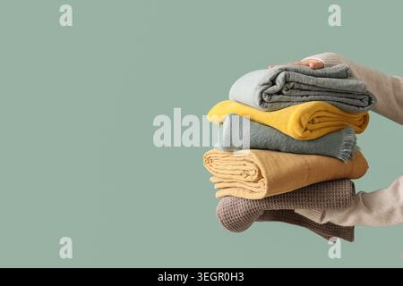 Female hands with stack of different blankets on turquoise background Stock Photo