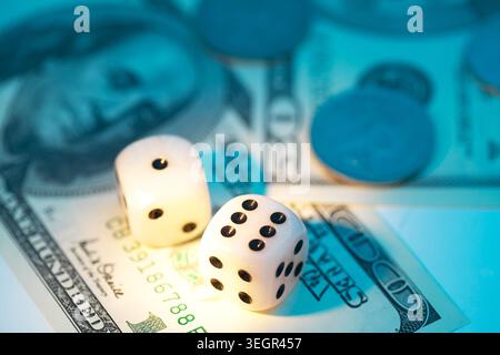 Two white dice sit on top of a $100 bill, surrounded by playing cards and poker chips. Stock Photo