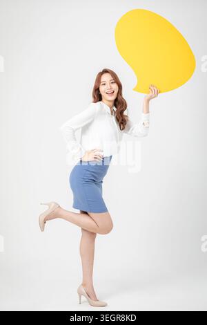 A young woman holding a yellow speech bubble, smiling and looking directly at the camera. Stock Photo