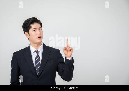 A young Asian businessman points upwards, lost in thought. Stock Photo
