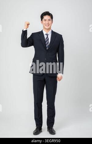 A young Asian man in a suit and tie, smiling and flexing his right arm. Stock Photo