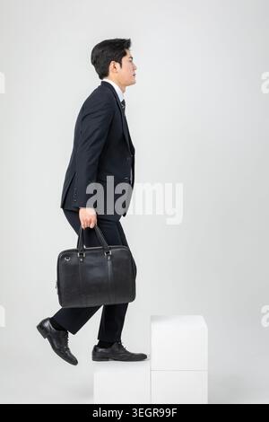 A businessman in a suit steps out of a white cube, carrying a briefcase and looking forward. Stock Photo