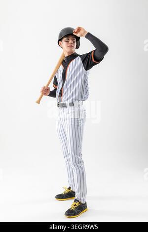 A young baseball player in uniform, holding a bat and adjusting his helmet. Stock Photo