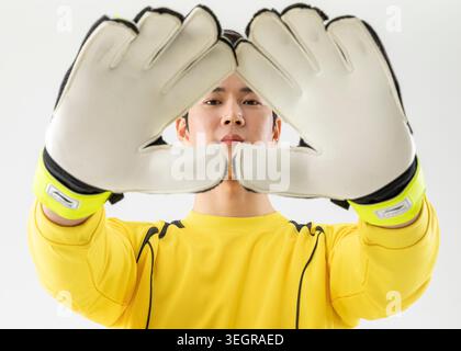 A goalkeeper is shown in a split-screen pose, focusing on his hands in front of his face, with a neutral expression. Stock Photo