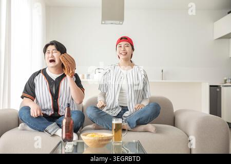 Two friends watching a baseball game together on a couch, laughing and having a good time. Stock Photo
