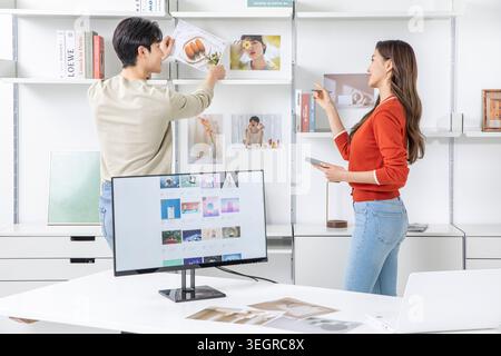 A young male and female are browsing through a digital image library in a modern, white studio, selecting and editing images. Stock Photo