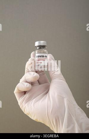 A hand in a white glove holds a vial of COVID-19 vaccine. Stock Photo