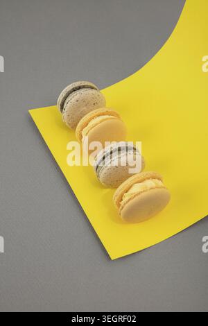 A row of colorful macarons on a yellow piece of paper, arranged in a curved line. Stock Photo