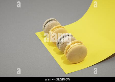 A row of macarons of various flavors is arranged on a bright yellow paper on a neutral grey background. Stock Photo
