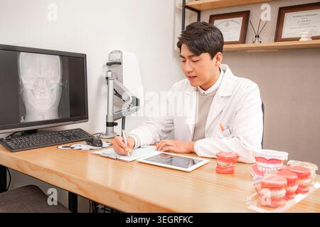 A young male doctor in a white lab coat studies a patient's X-ray on a computer screen in a modern dental clinic. Stock Photo