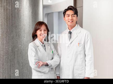 Two medical professionals in white coats smiling and standing in a hospital corridor. Stock Photo