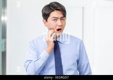 A man in a business suit is covering his mouth with his hand, looking surprised and concerned in a modern office setting. Stock Photo