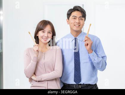Two smiling office workers in business attire hold toothbrushes in a bright, modern office. Stock Photo
