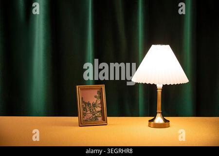A vintage lamp sits on a table next to a gold-framed picture, both casting warm light in a quiet, elegant room. Stock Photo