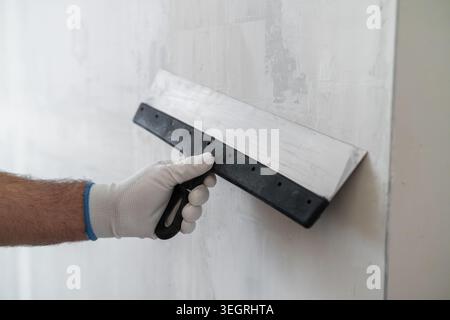 A professional is smoothing joint compound on a drywall surface using a hand trowel. The workspace features well prepared plasterboard and clean edges visible in the background. Stock Photo