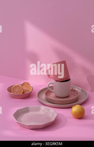 A stack of pink and white ceramics and a bowl of citrus slices on a pink tablecloth. Stock Photo