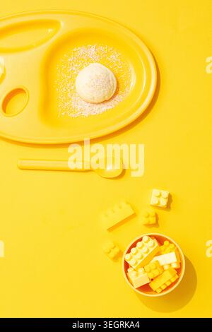 A bowl of colorful building blocks and a plate of ice cream are arranged on a bright yellow table. Stock Photo