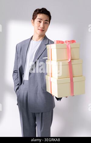 A young Asian man in a suit holds a stack of gift boxes with a pink ribbon. Stock Photo
