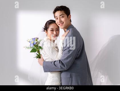 A young couple in formal attire share a tender moment, embracing in a sunny, white-painted studio. Stock Photo