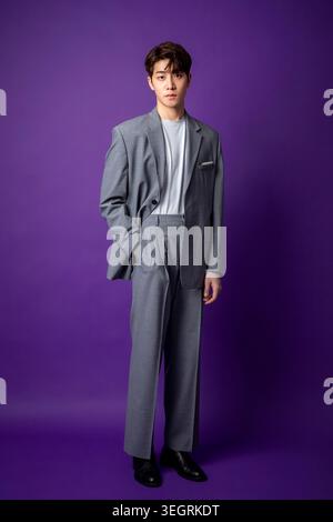 A young Asian man in a business suit stands confidently against a vibrant purple background. Stock Photo
