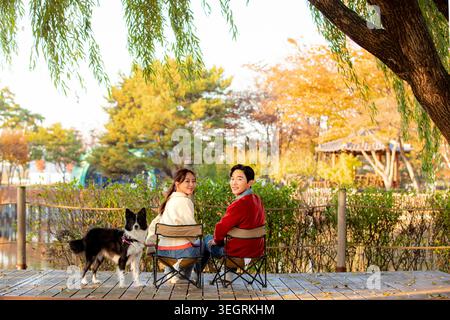 A couple and their dog sit on a park bench, enjoying a sunny afternoon together. Stock Photo