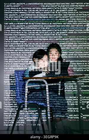 Two students in a darkened classroom, using a laptop to explore a code-heavy website. Stock Photo