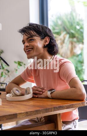 Man sitting at table at home leaning smiling in pink top and headphones near mic boom Stock Photo