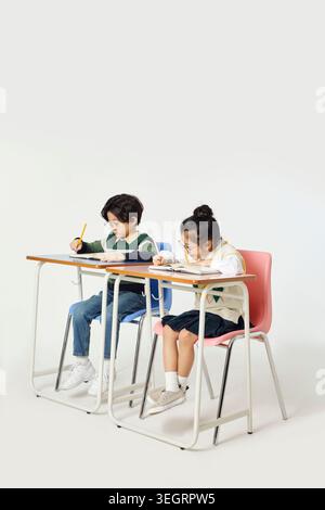 Two children in glasses sit at a desk, studying and taking notes in a classroom setting. Stock Photo