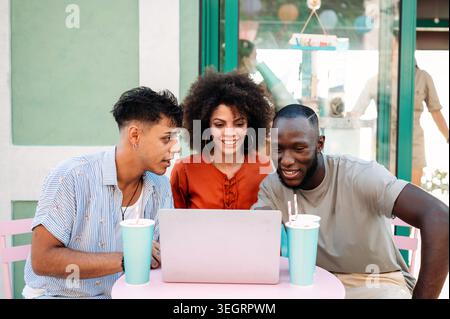 Multicultural startup team enjoys a relaxed outdoor meeting, collaborating over a laptop, having fun Stock Photo