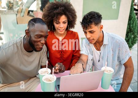 Multicultural startup team enjoys a relaxed outdoor meeting, collaborating over a laptop, having fun Stock Photo