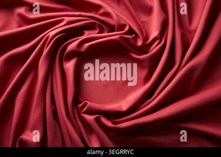 A deep red silk fabric is swirled and ruffled, revealing its smooth, shiny surface. Stock Photo