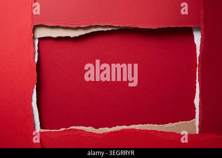 A torn piece of red paper is revealed through a gap in a larger red sheet. Stock Photo