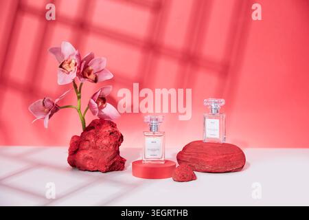 A pink orchid stands tall among two glass perfume bottles on a white surface. Stock Photo