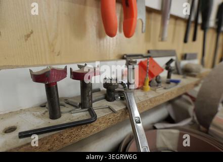 Various tools including forstner bits, an adjustable wrench, and other drilling and fastening equipment are neatly arranged on a wooden shelf in a woo Stock Photo