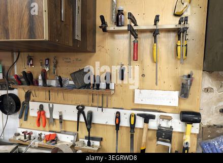 Workshop tools, including hammers, screwdrivers, clamps, and pliers, neatly organizing on a wooden pegboard wall, showing a practical workspace for di Stock Photo