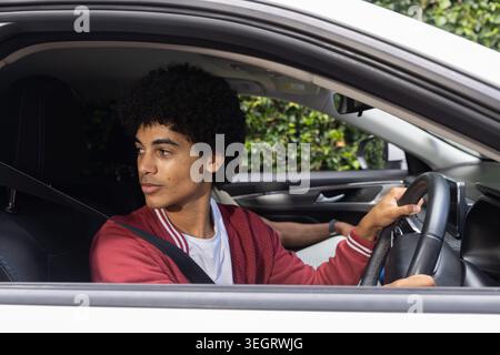 African American man sitting in car wearing red jacket, holding wheel, seatbelt on looking left Stock Photo